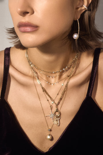 Close-up of a woman wearing multiple necklaces with a neutral background
