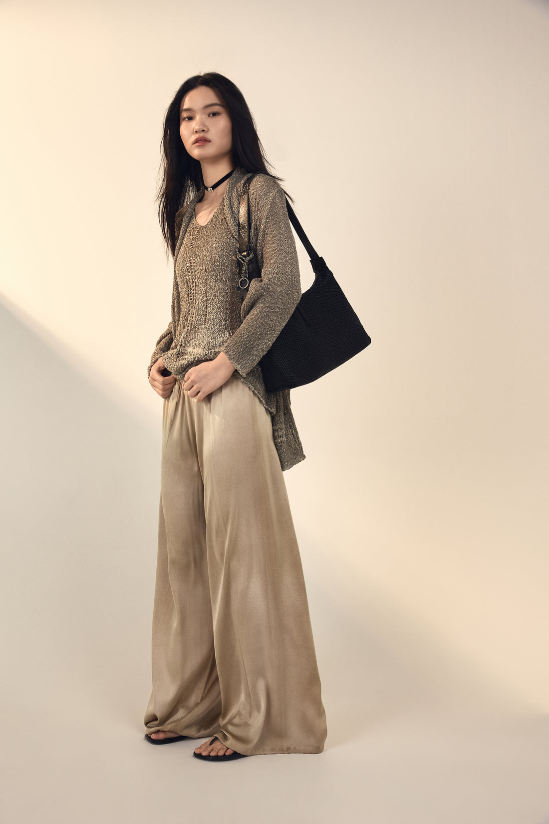 Woman wearing a beige outfit with a black handbag on a plain background