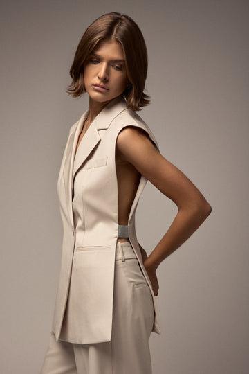 Woman wearing a beige sleeveless blazer and pants against a neutral background