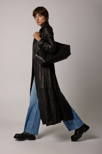 Person wearing a black leather coat over a blue denim outfit on a plain background